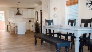 Una cocina moderna con armarios blancos, electrodomésticos de acero inoxidable y una zona de comedor con mesa y sillas de madera.