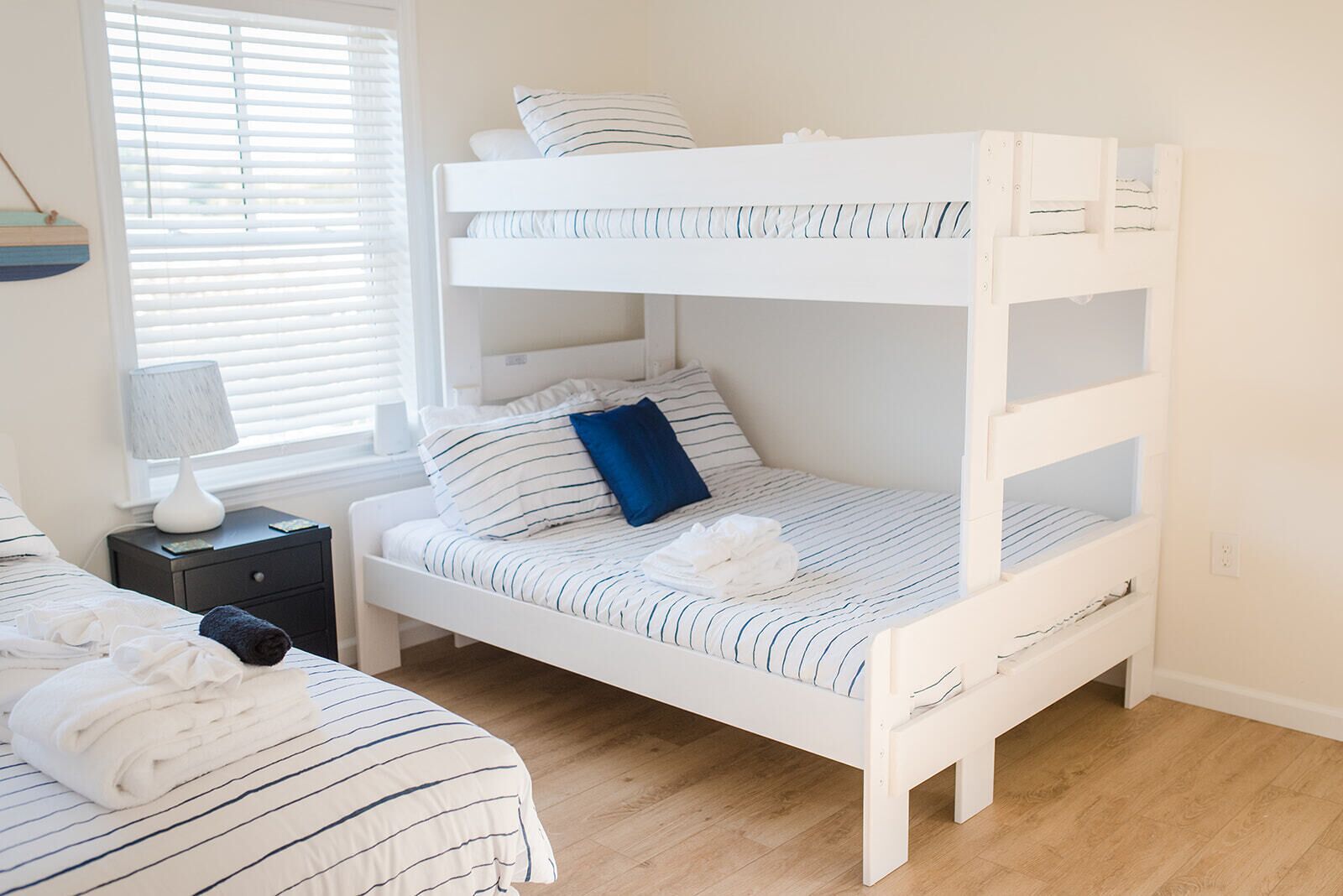 Una cama litera con ropa de cama a rayas, una mesita de noche con una lámpara y una ventana con persianas.