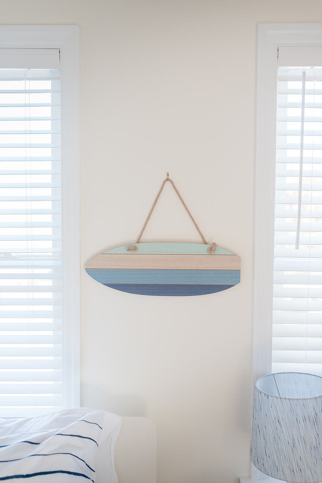 A room with a bed, a hanging wooden shelf, and a lamp.