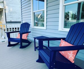 Twee Adirondack stoelen met zeesterenkussens op een houten terras.