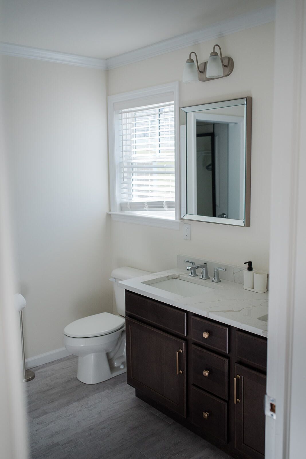 A bathroom with a toilet, a sink with a mirror, and a window with blinds.