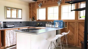 A kitchen with a central island, bar stools, wooden walls, and large windows. - Rustic Chic Maine Cabin (Sedgwick)