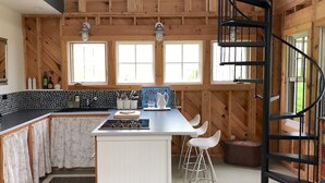 A kitchen with a central island, bar stools, a spiral staircase, and a stone backsplash. - Rustic Chic Maine Cabin (Sedgwick)