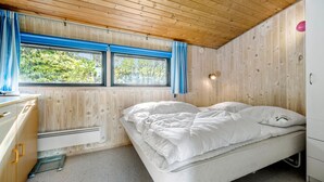 Ein gemütliches Schlafzimmer mit Holzboden, einem Bett mit weißer Bettwäsche, einem kleinen Schreibtisch und einem Fenster mit blauen Vorhängen.