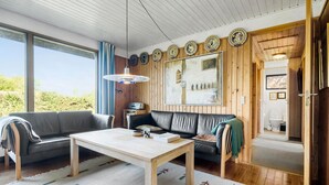 Ein gemütliches Wohnzimmer mit Holzbalkendecke, einer schwarzen Ledersofa, einem Couchtisch aus Holz und einem großen Fenster mit Vorhängen.