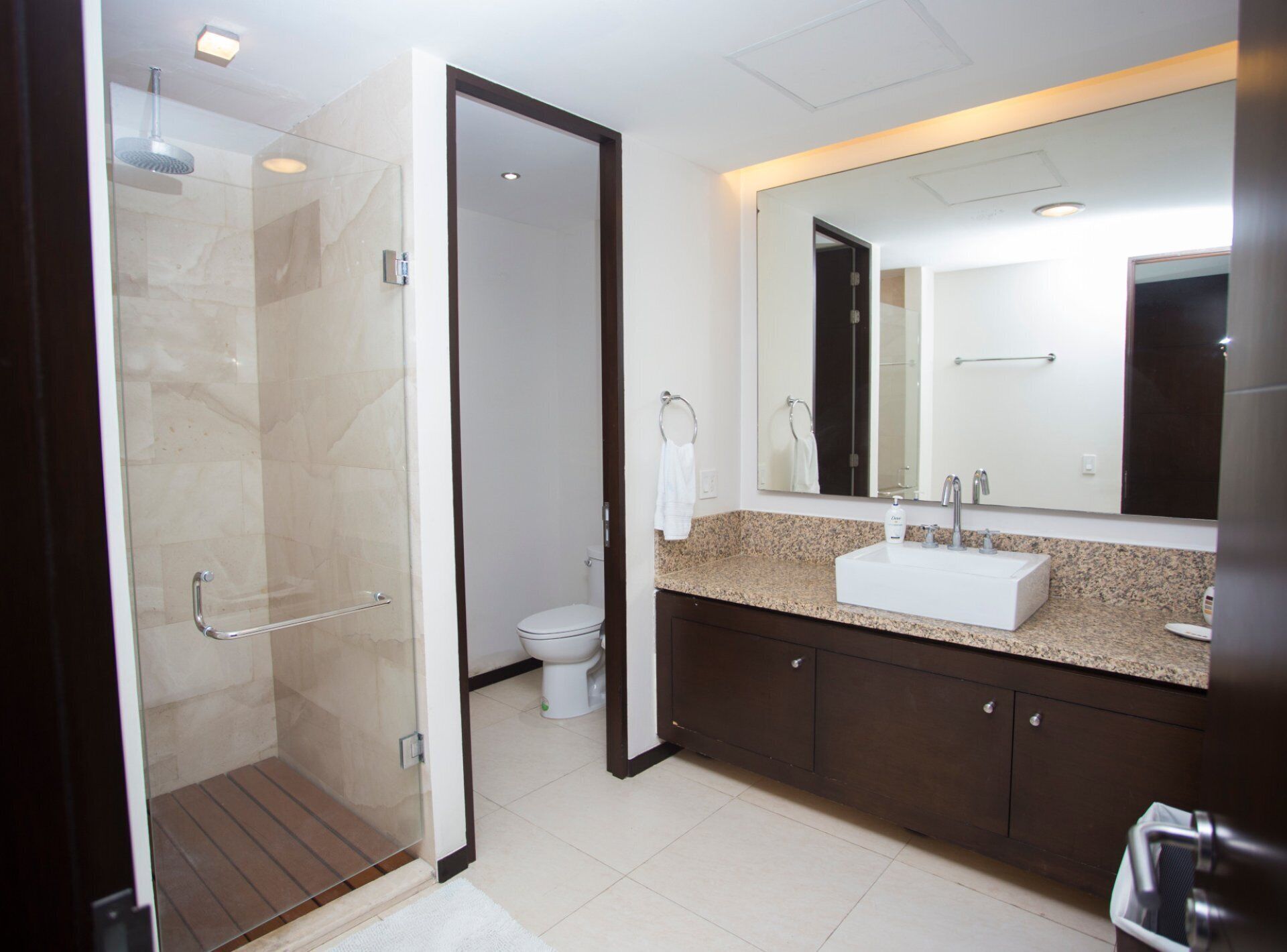 Een moderne badkamer met een douche met glazen wand, een grote spiegel en een granieten aanrechtblad.