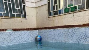 Een buitenzwembad met helderblauw water, betegelde wanden en een blauwe bal.