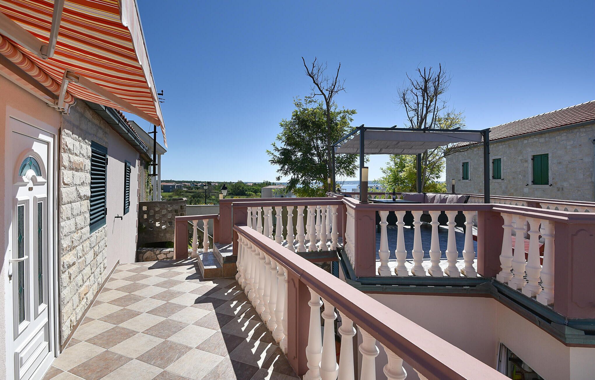 A balcony with a checkered floor, white balustrade, and a view of a coastal area.