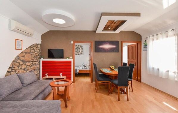 Un espace de vie compact comprenant un canapé, une table à manger avec des chaises, un téléviseur, un meuble rouge, un mur en pierre et un plafond en bois.