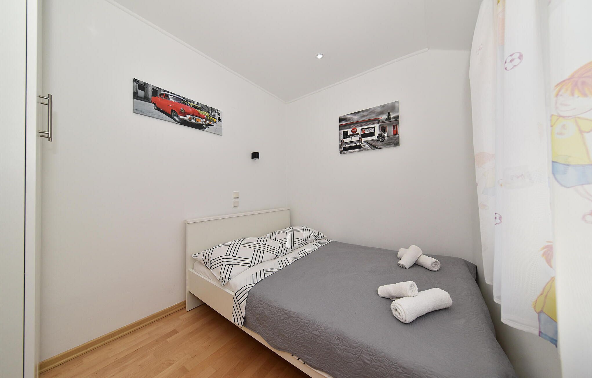 Een compacte, netjes ingerichte slaapkamer met een enkel bed, een hoofdeinde en twee aan de muur bevestigde foto’s.