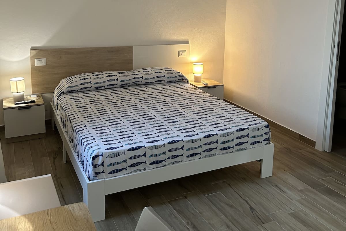 Un dormitorio con cama, mesitas de noche, una silla, un equipo de aire acondicionado y un aplique de pared.