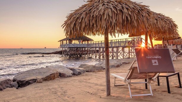 A beach with a thatched umbrella, a wooden pier, and a lounge chair with a sign. - Stella di Mare rent rooms (Civitavecchia)