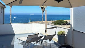 An outdoor patio with a table, chairs, and a large umbrella. There is a view of the sea and a ship in the distance. - Stella di Mare rent rooms (Civitavecchia)