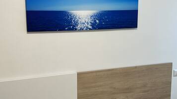 Una stanza con un letto in legno, una parete bianca e un quadro che raffigura un cielo azzurro e l'oceano.