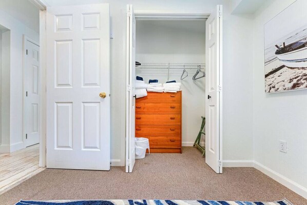 Un couloir mène à un placard contenant une commode en bois et des vêtements suspendus.