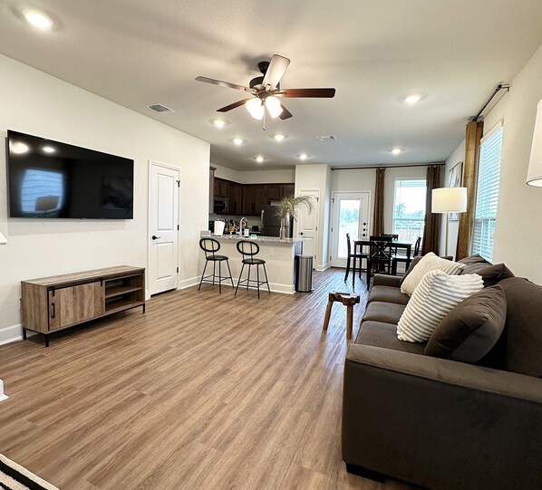A modern living room with a brown sofa, a TV mounted on the wall, and a ceiling fan.