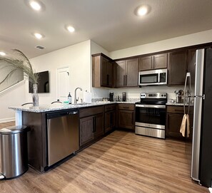 A modern kitchen with wooden cabinets, stainless steel appliances, a granite countertop, and a wooden floor.