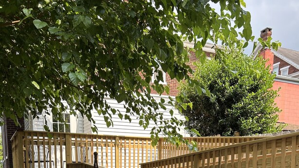 A wooden deck with a wooden fence, a garden with various plants, and a brick building in the background.
