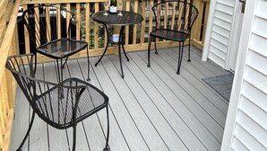 A wooden deck with two metal tables and chairs, a bottle of wine, and a lantern.