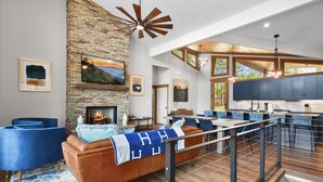 Una sala de estar moderna con chimenea de piedra, sofás azules y techo de madera.