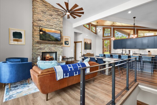A modern living room with a stone fireplace, blue sofas, and a wooden ceiling. - Mountain Oasis ~ PRIVATE outdoor pool, pickleball/basketball court, fire pit, hot tub, views! (Ellijay)