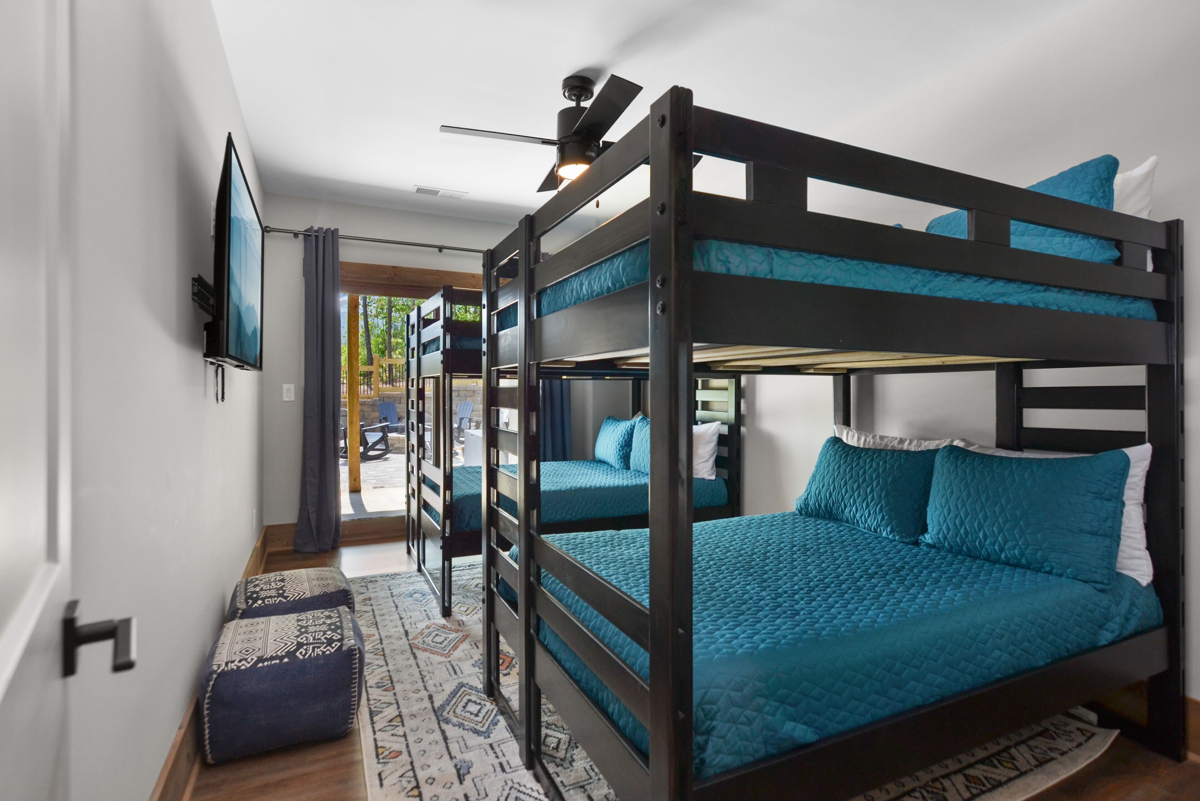 A bunk bed room with a ceiling fan, a television, and a patterned rug.