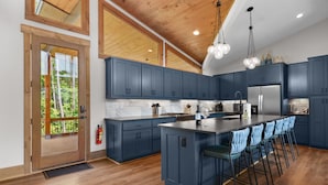 Una cocina moderna con armarios azul oscuro, una isla grande con taburetes de bar, piso de madera y techo de madera.