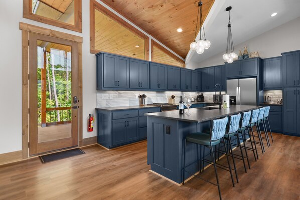 Een moderne keuken met donkerblauwe kastjes, een groot eiland met barstoelen, houten vloeren en een houten plafond.