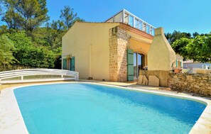 Blick auf einen Pool, ein Gebäude mit steinverkleideter Fassade, einem Glasbalkon und einer Steinmauer.