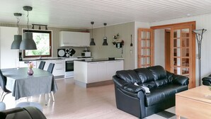 Ett modernt kök med vita skåp, ett matbord med stolar, en svart lädersoffa och en trädörr.