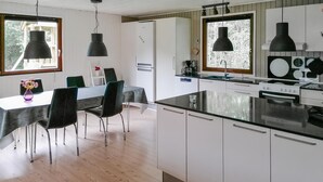 Ett modernt kök med vita skåp, en svart bänkskiva och hängande lampor. Det finns också en matplats med ett bord och stolar.