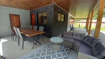 Un espace de restauration extérieur moderne, agrémenté d’un mur en pierre, d’un plafond en bois et d’un tapis à motifs gris.