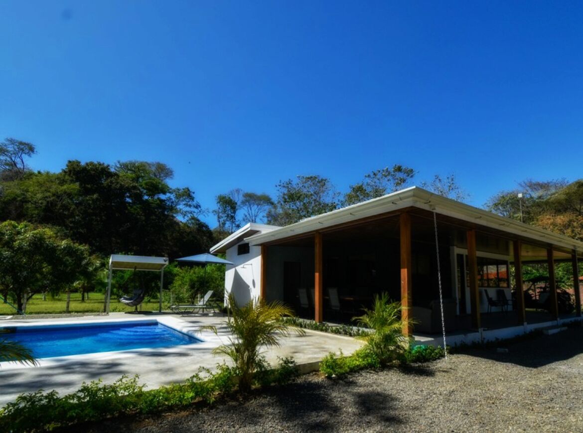 Una casa moderna con piscina, patio cubierto y exuberante vegetación.