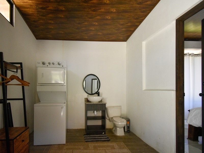 Une petite salle de bain avec des toilettes blanches, un petit lavabo, un miroir et un lave-linge blanc.