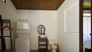 Une petite salle de bain avec des toilettes blanches, un petit lavabo, un miroir et un lave-linge blanc.
