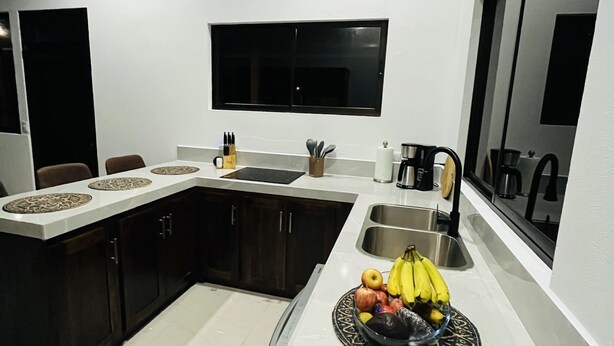 A modern kitchen with dark cabinets, a white countertop, and a built-in sink. - Comfort in the Jungle (Sámara)