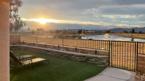 Une terrasse avec une pelouse, une piscine et une vue sur un paysage au coucher du soleil.