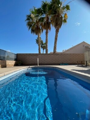 A swimming pool with clear blue water, surrounded by a brick wall and palm trees.