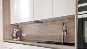 Eine moderne Küche mit weißen Schränken, einer Holz-Spritzschutzwand, einer Edelstahl-Spüle und einer Standmixer.