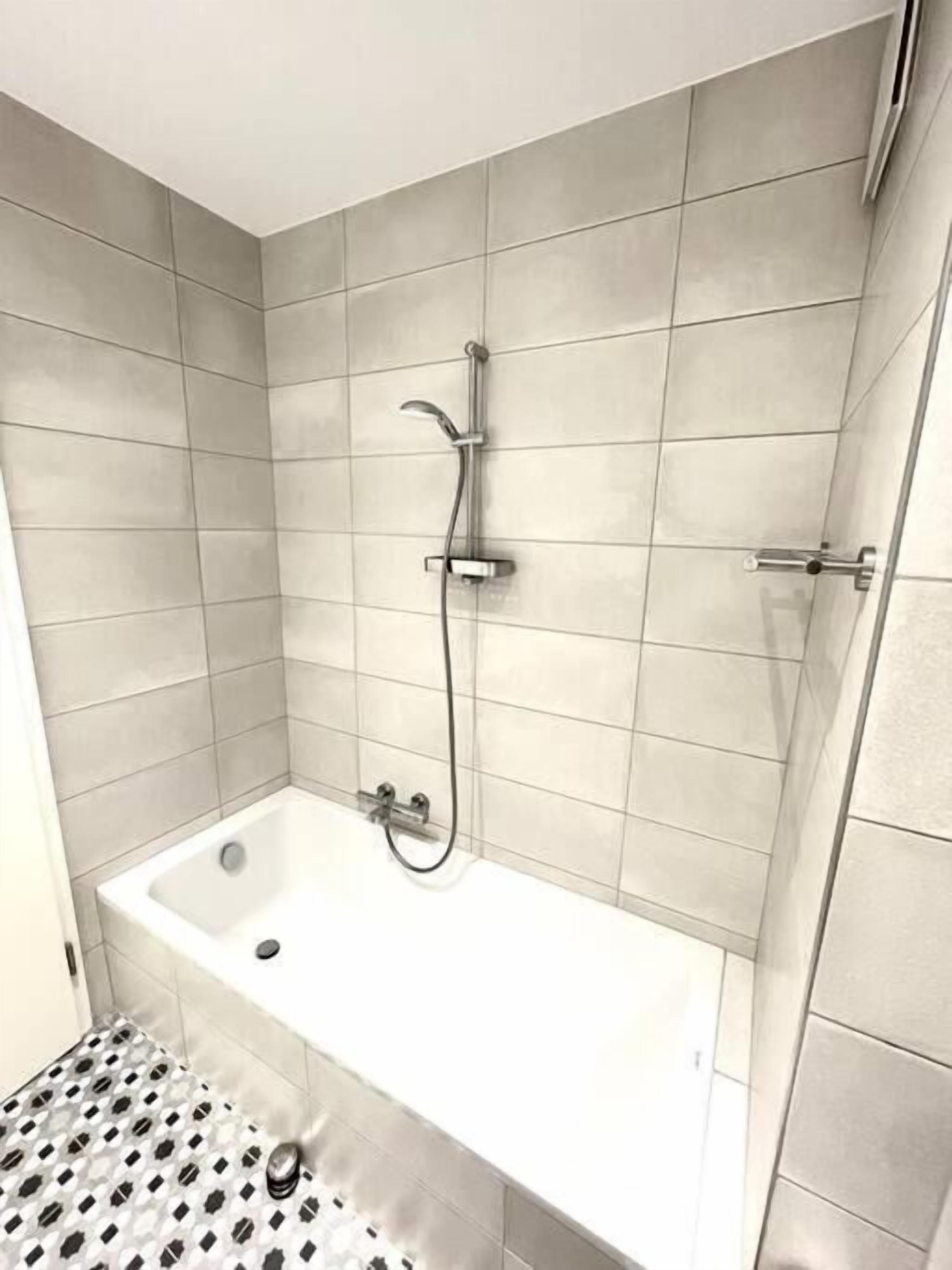 Un baño pequeño y moderno con ducha, bañera y retrete. Las paredes están cubiertas de azulejos y el suelo tiene un diseño estampado.