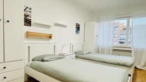 Ein Schlafzimmer mit zwei Betten, einem Kleiderschrank, einem Heizkörper und einem Fenster mit Vorhängen.