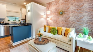 Una cocina moderna con una isla azul, un sofá blanco con cojines amarillos y una pared decorativa con un diseño ondulado.