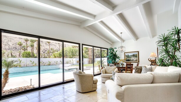 A spacious living room with large windows, a pool, and a view of a landscaped area. - Private Pool & Spa: Indian Wells Home! (Indian Wells)