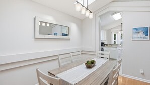 Un coin repas avec une table en bois, des chaises blanches, un miroir et un tableau accroché au mur.