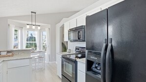 Une cuisine moderne avec des meubles blancs, un réfrigérateur noir, un four à micro-ondes et un four encastré.