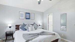 Une chambre à coucher moderne avec un grand lit, des lampes de chevet, un ventilateur de plafond et des œuvres d’art encadrées accrochées au mur.
