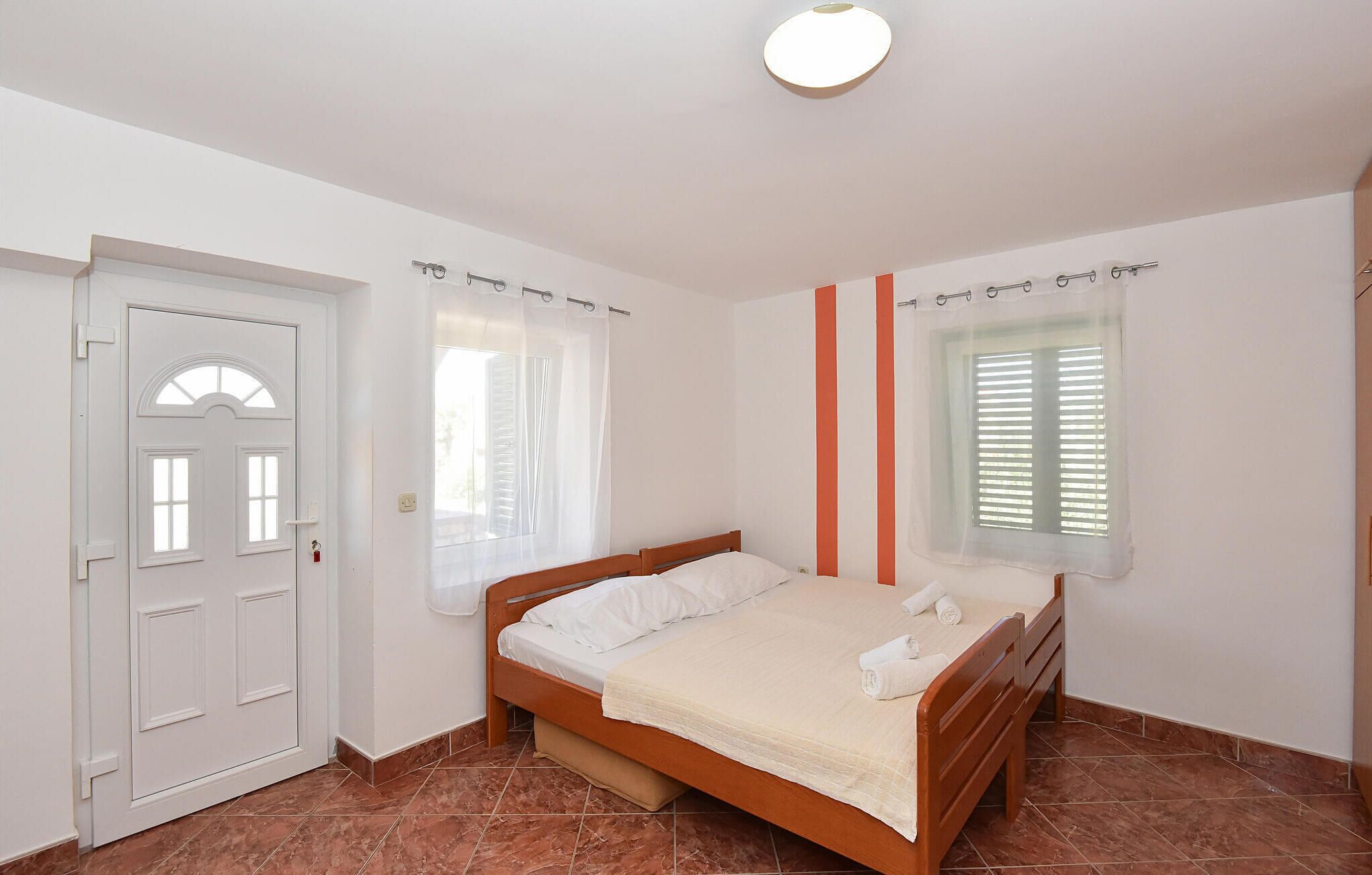 A bedroom with a bed, a door, a window with blinds, and a light fixture.