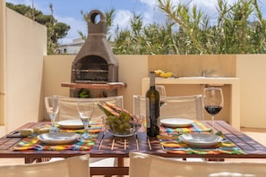 Un espace de restauration en plein air avec un four à pizza, une bouteille de vin et un saladier de fruits.