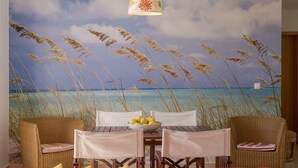 A room with a beach mural, a dining table with chairs, and a bed with red bedding.