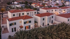 A residential area with modern white buildings, red-tiled roofs, and a dense cluster of palm trees.